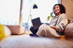 a woman holding a laptop while leaning on a couch 