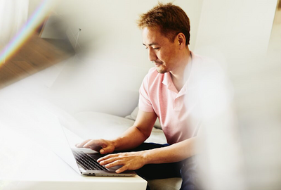 a man wearing a pink shirt typing in his laptop
