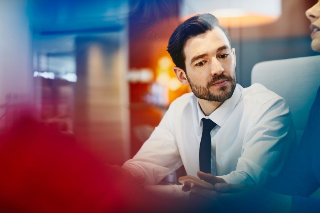 a man wearing a white button up shirt and tie looking at his coworker's work