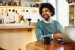 A photo of a man smiling while looking to the left while his hands are on the keyboard of his laptop