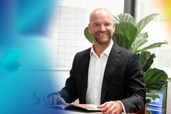 a bearded man wearing a suit while smiling and looking to the right
