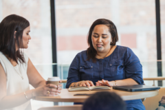 two maori women going over work and drinking coffee