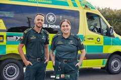 an image of a man and woman in their uniforms working at st john with their vehicle at the back