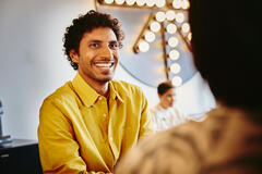 an image of a man wearing a yellow collared shirt smiling brightly at his female friend
