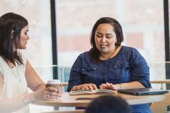 two maori women going over work and drinking coffee