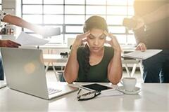 an image of a woman holding her temples with her laptop beside her