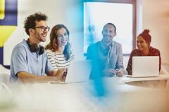 a team with laptops in front of them discussing something while smiling