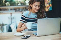 a young woman holding a cup while working on something on her laptop