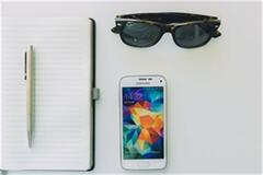an image of a notebook with pen, sunglasses and phone