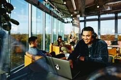 Smiling man with headphones and laptop sitting in a lounge environment.