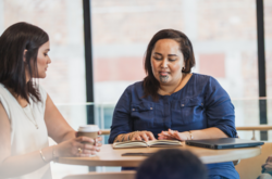 two maori women going over work and drinking coffee