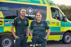 an image of a man and woman in their uniforms working at st john with their vehicle at the back