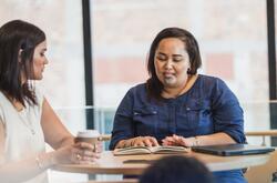 two maori women going over work and drinking coffee