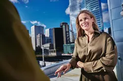 Female smiling, standing outside on a balcony talking to a person