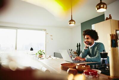 A man with a laptop resting his chin on his palm while smiling at something far away