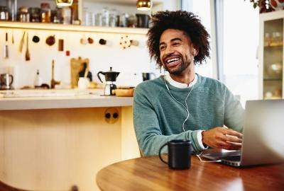 A photo of a man smiling while looking to the left while his hands are on the keyboard of his laptop