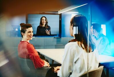 three people in a conference room having a meeting with a person who on the tv screen having a meeting 