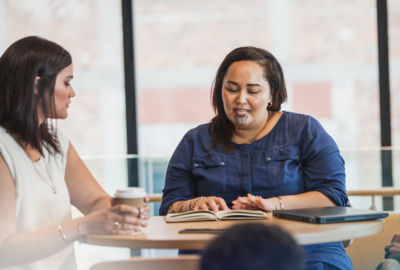 two maori women going over work and drinking coffee