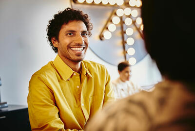 an image of a man wearing a yellow collared shirt smiling brightly at his female friend