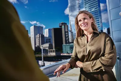 Female smiling, standing outside on a balcony talking to a person