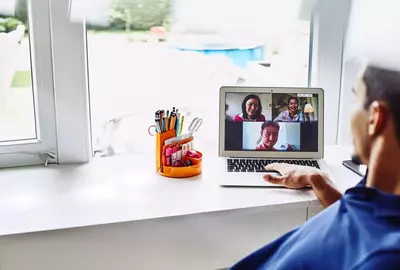 male working from home on laptop, meeting with colleagues in a video call.
