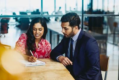 a woman writing something while discussing something to her coworker