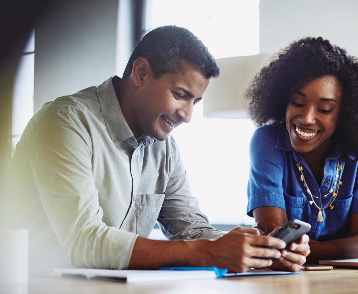 a man looking at something on his phone while his coworker is leaning for a look as well