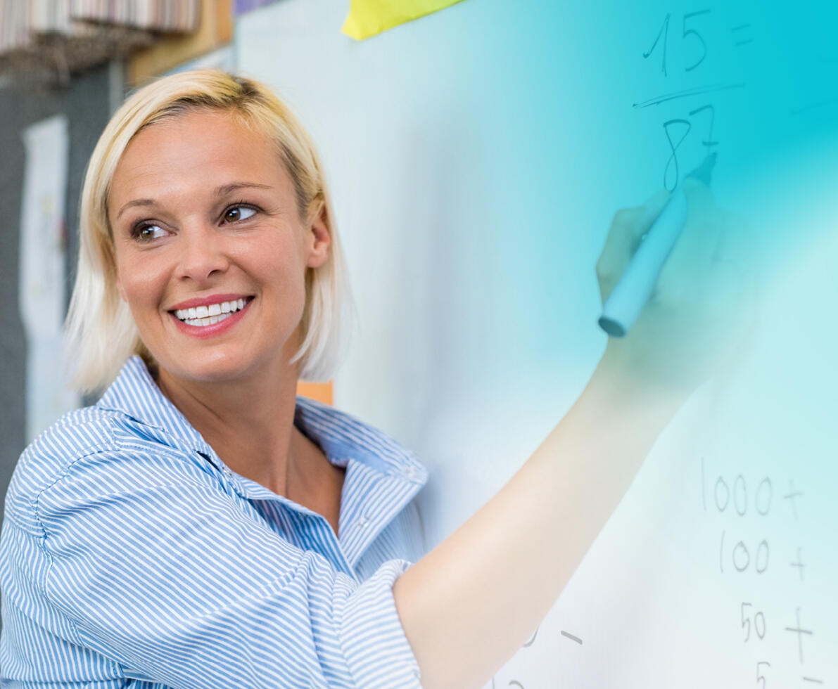 A photo of a smiling teacher writing on a whiteboard