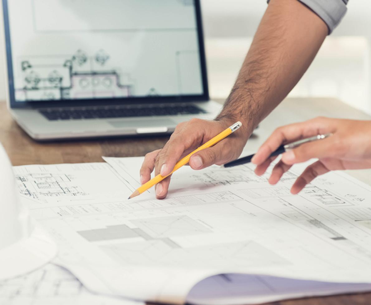 A photo of two people working in construction checking out the floor plan with a laptop on the desk