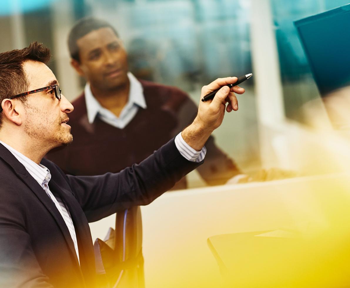 A photo of two men in an office with one pointing at a computer screen