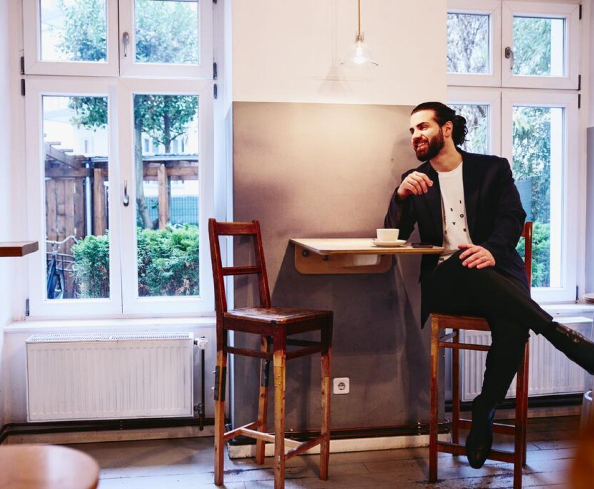 Man sitting at table with a coffee, smiling looking away.