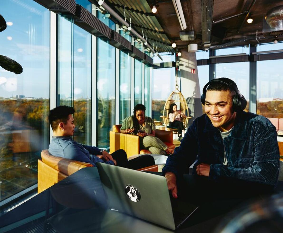 A photo of a man wearing headphones while smiling and looking at his laptop in a cafe