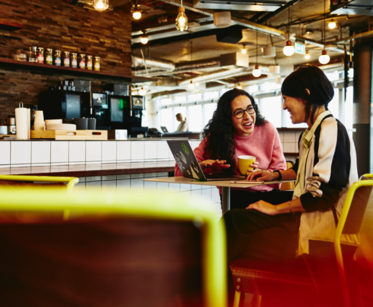 Two women chatting at a cafe with their laptop and coffee