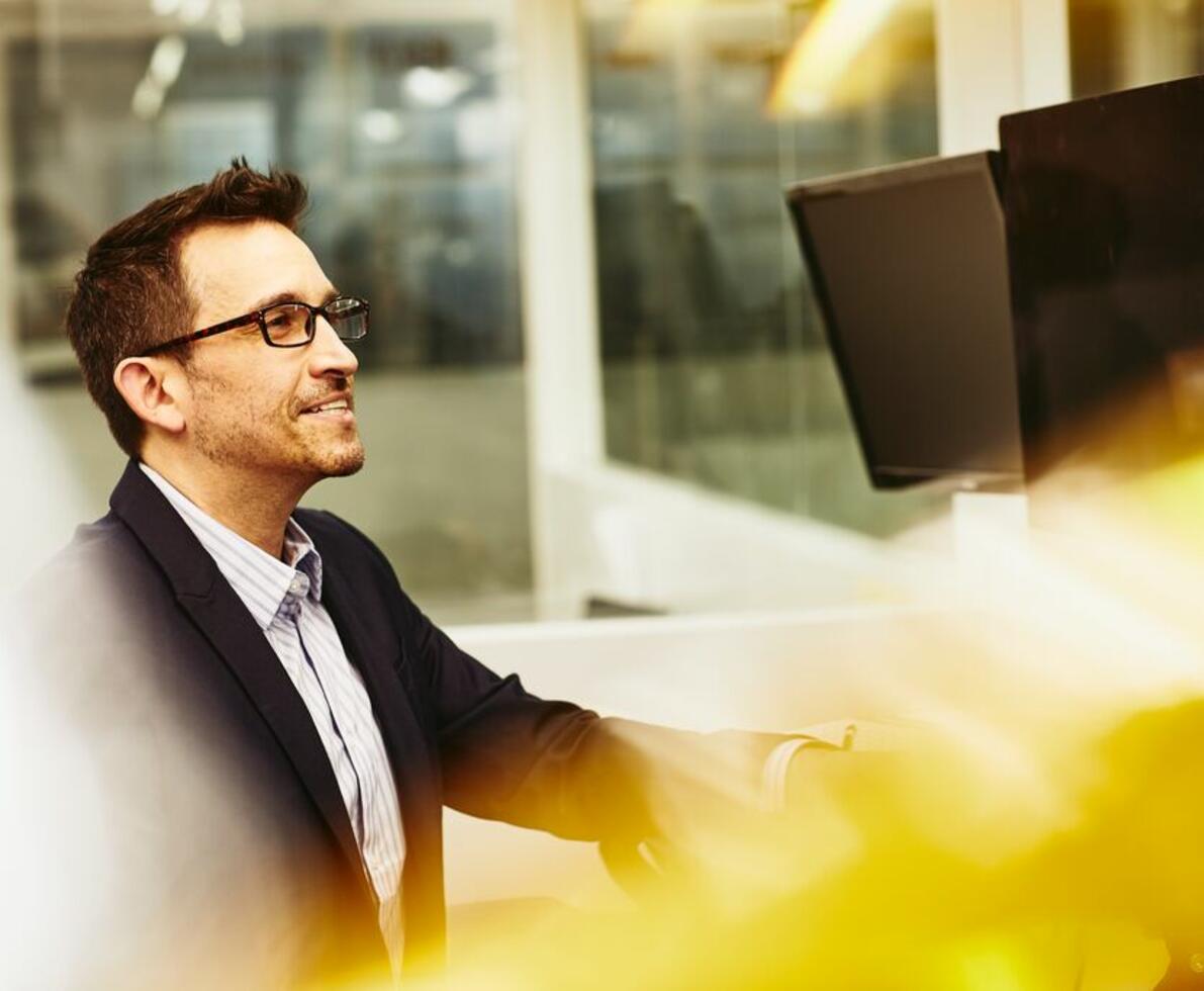 A man in a suit wearing glasses looking at his desktop screen smiling