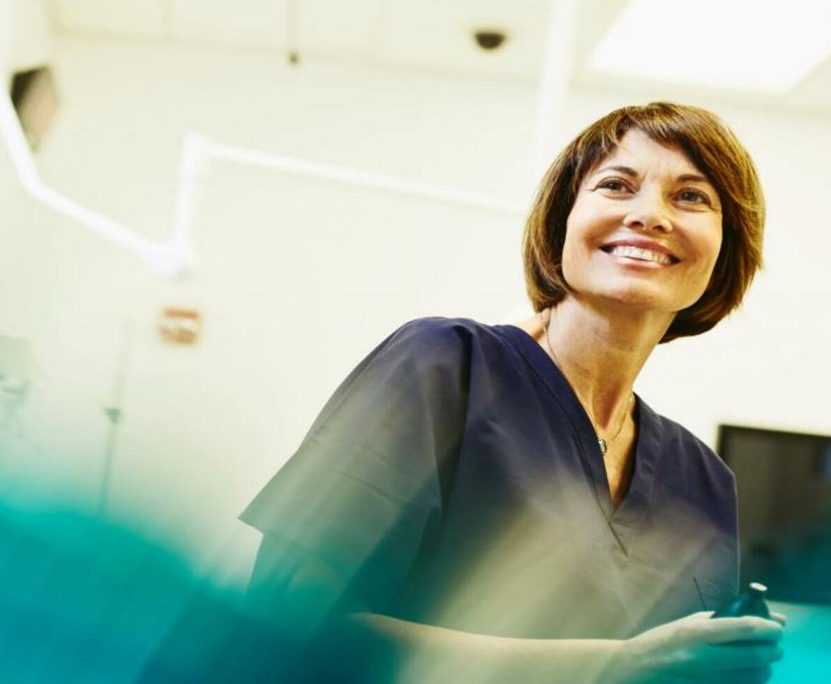 A female nurse smiling and looking to the far left inside a hospital room