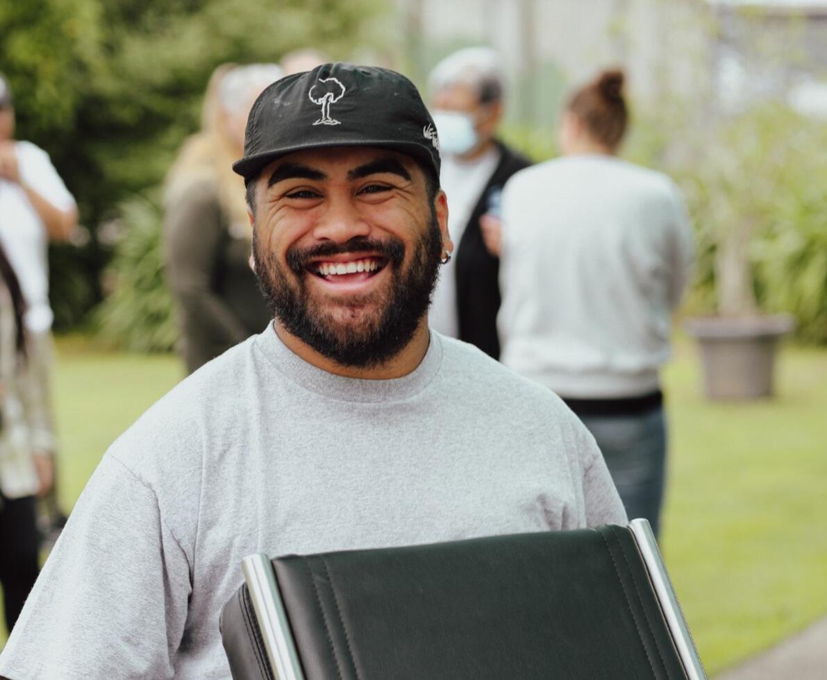 smiling man wearing a baseball cap standing in green space outdoors