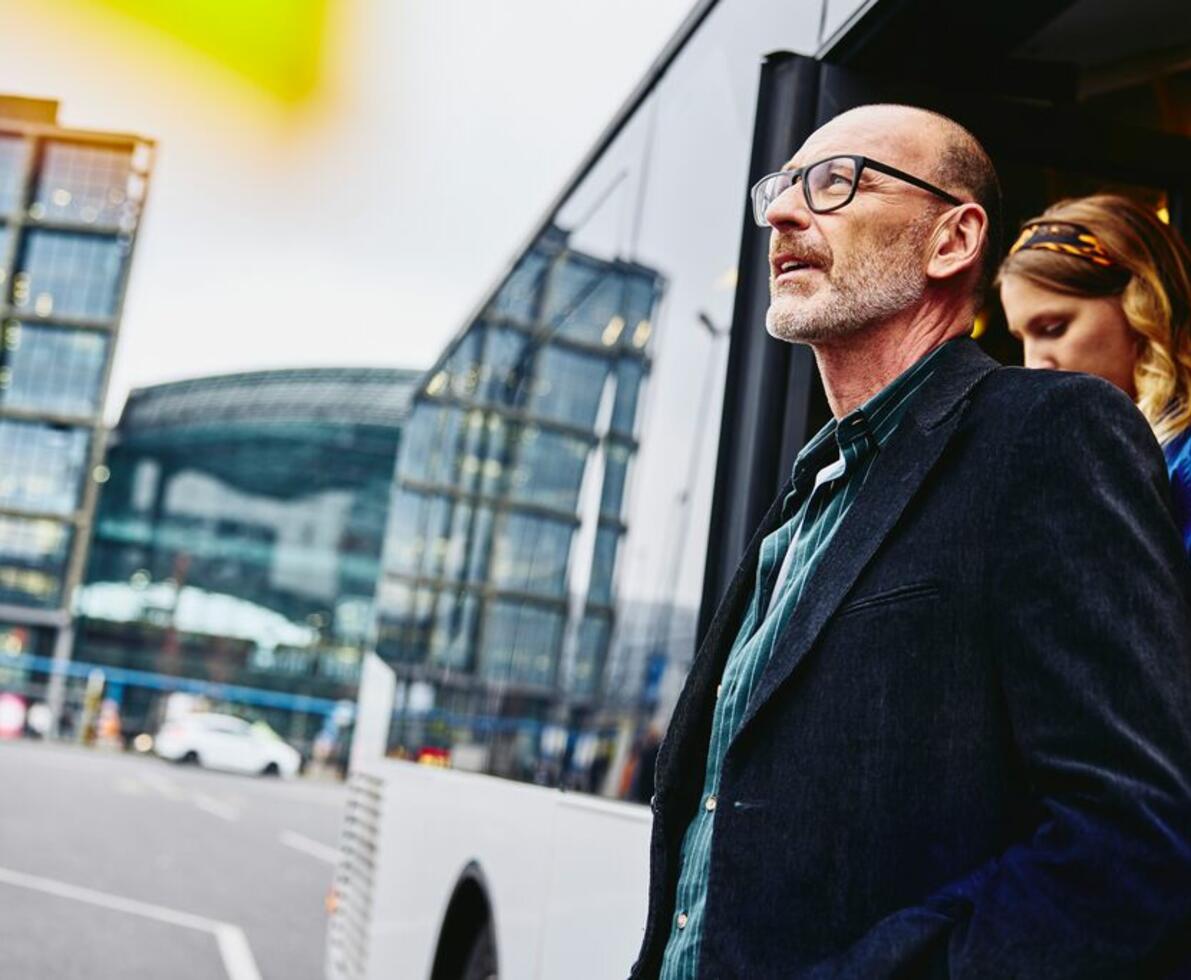 an older man with glasses exiting a bus while looking far to the left