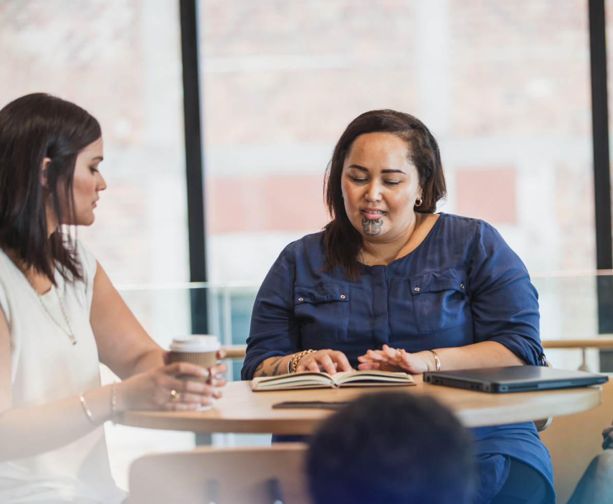 two maori women going over work and drinking coffee