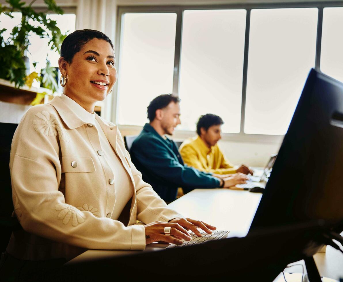 an image of a woman typing on her keyboard while smiling brightly and looking at something to her far left