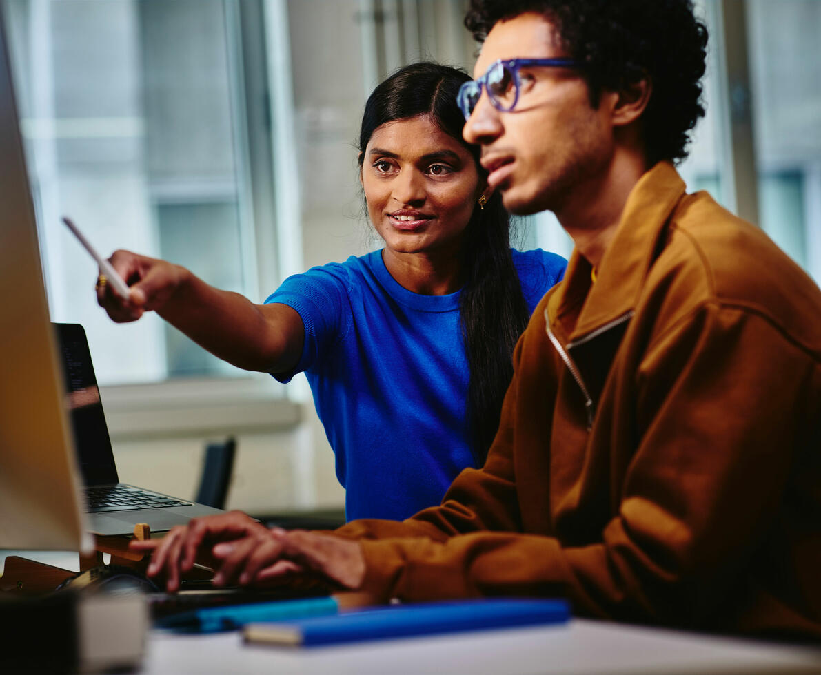 two people looking at a screen, woman pointing at the screen with her pen