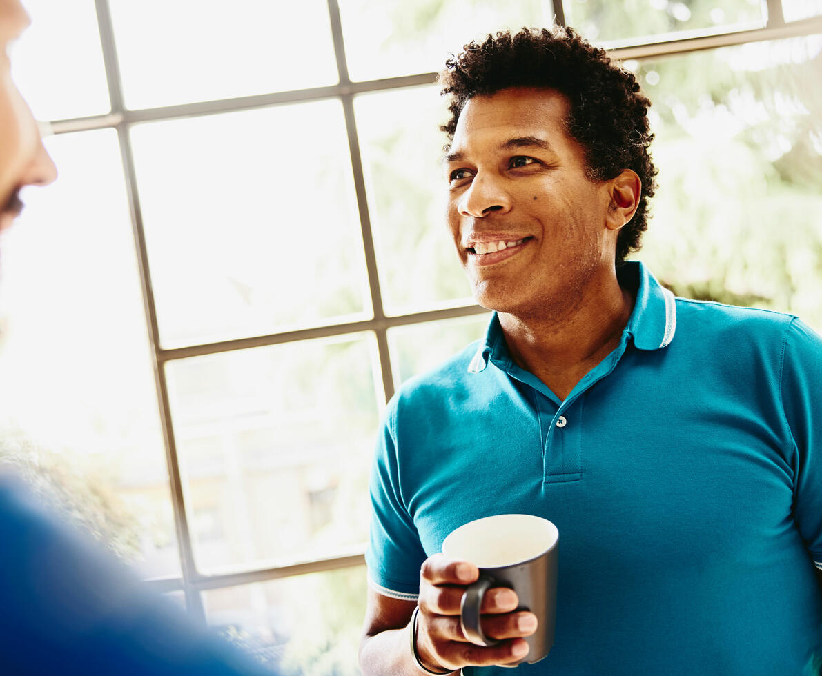 Smiling male holding a coffee cup having a chat with someone.