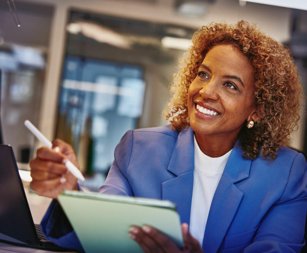 an image of a woman wearing a blue coat and white top smiling brightly while holding a tablet and pen