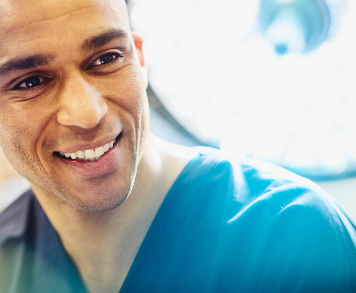 an image of a man wearing a nurse uniform smiling while looking to the right
