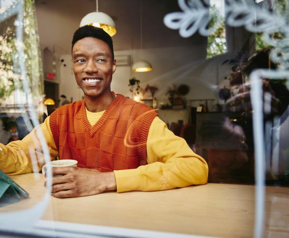an image of a man wearing an orange sweater smiling while looking to the right