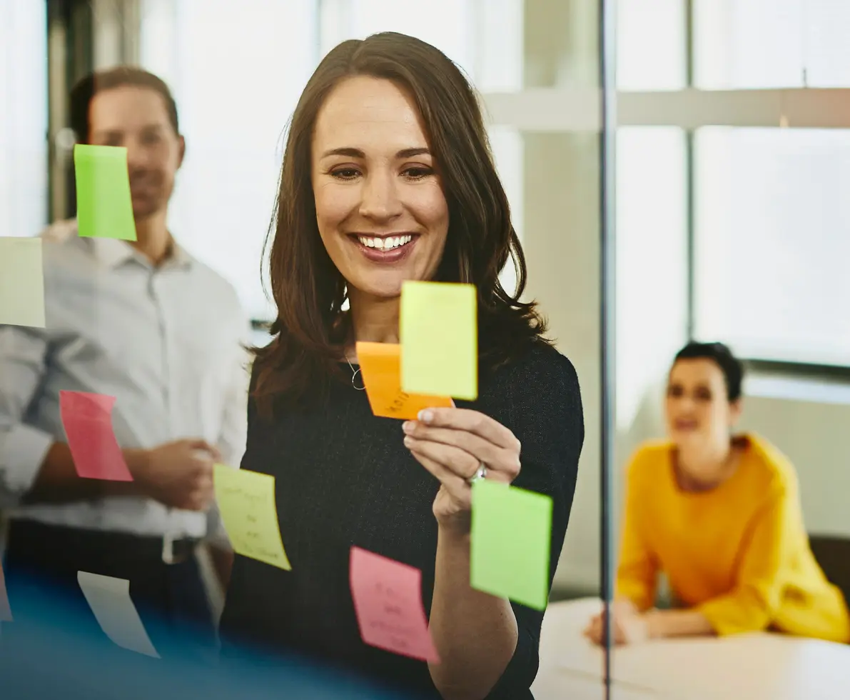 an image of a woman adding sticky notes in the transparent glass wall in their meeting room with her colleagues