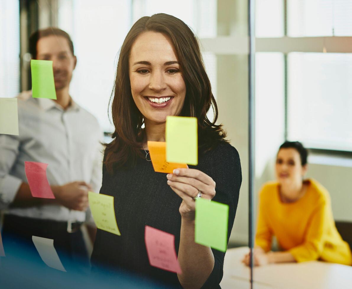 an image of a woman adding sticky notes in the transparent glass wall in their meeting room with her colleagues