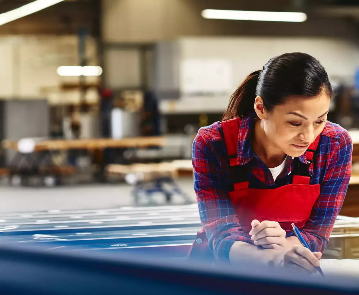 Womale wearing a red overall writing on a paper in a production site/factory.
