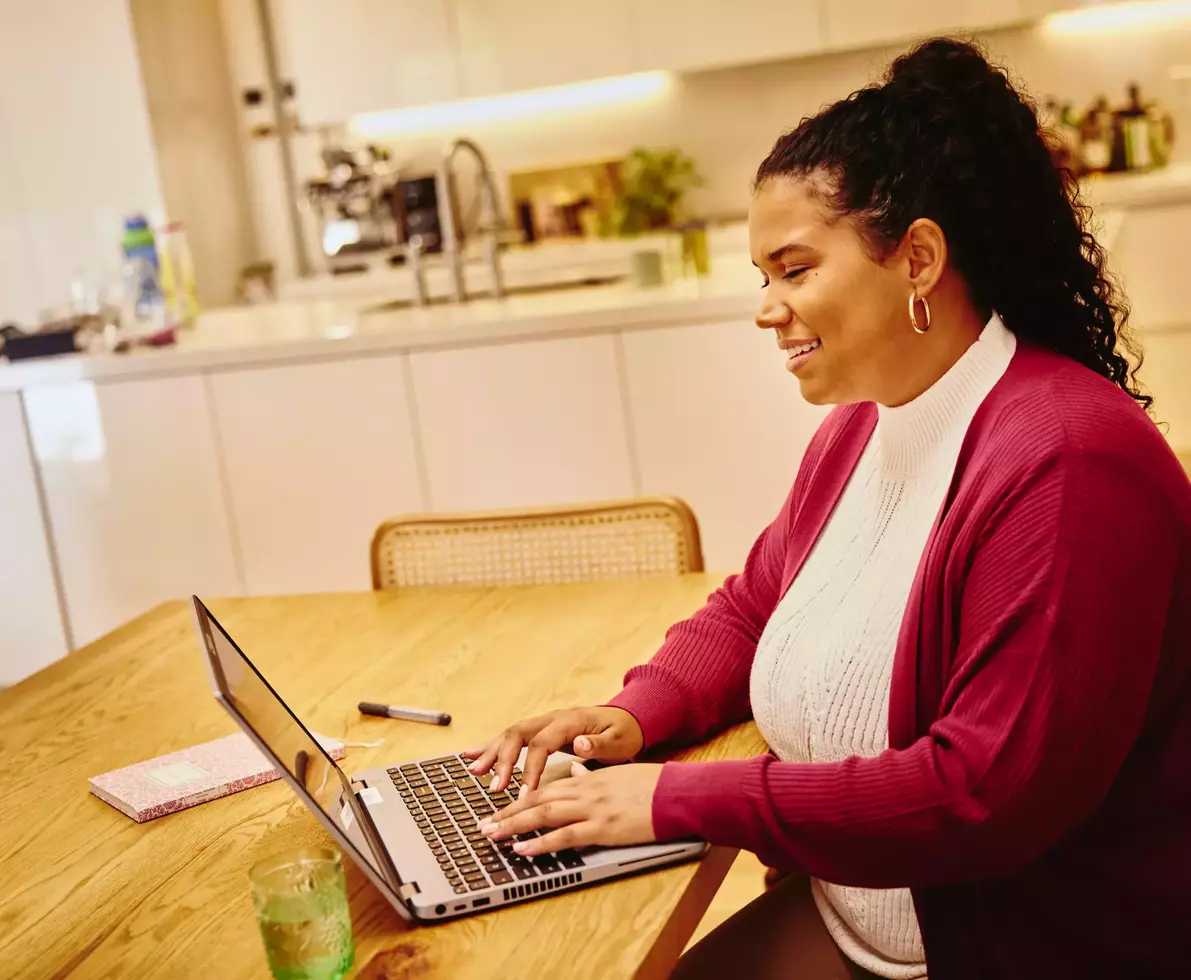 Female, smiling, working on laptop in kitchen on a kitchen table