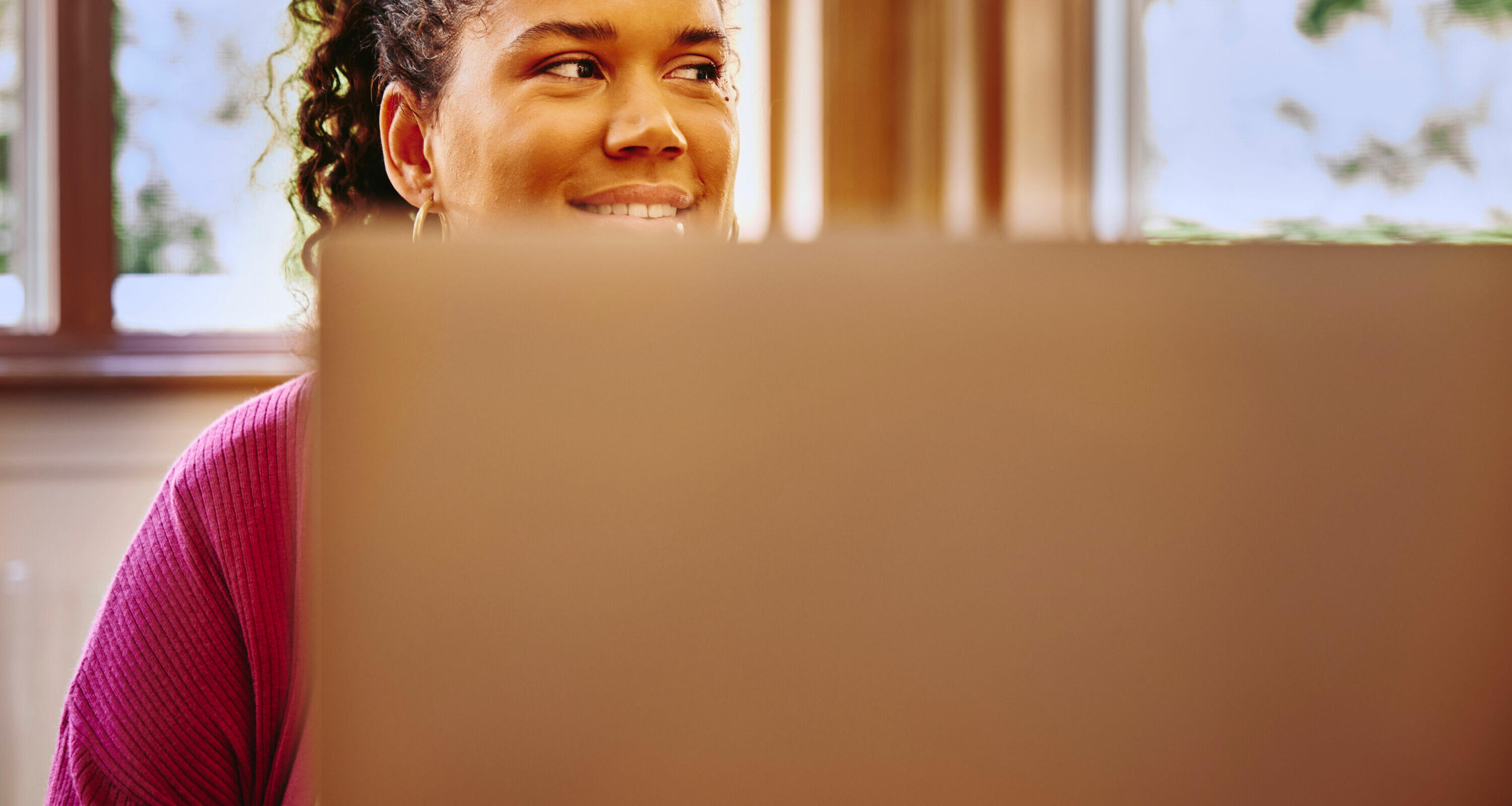 female, in a purple top, smiling, looking away with a laptop in front of her