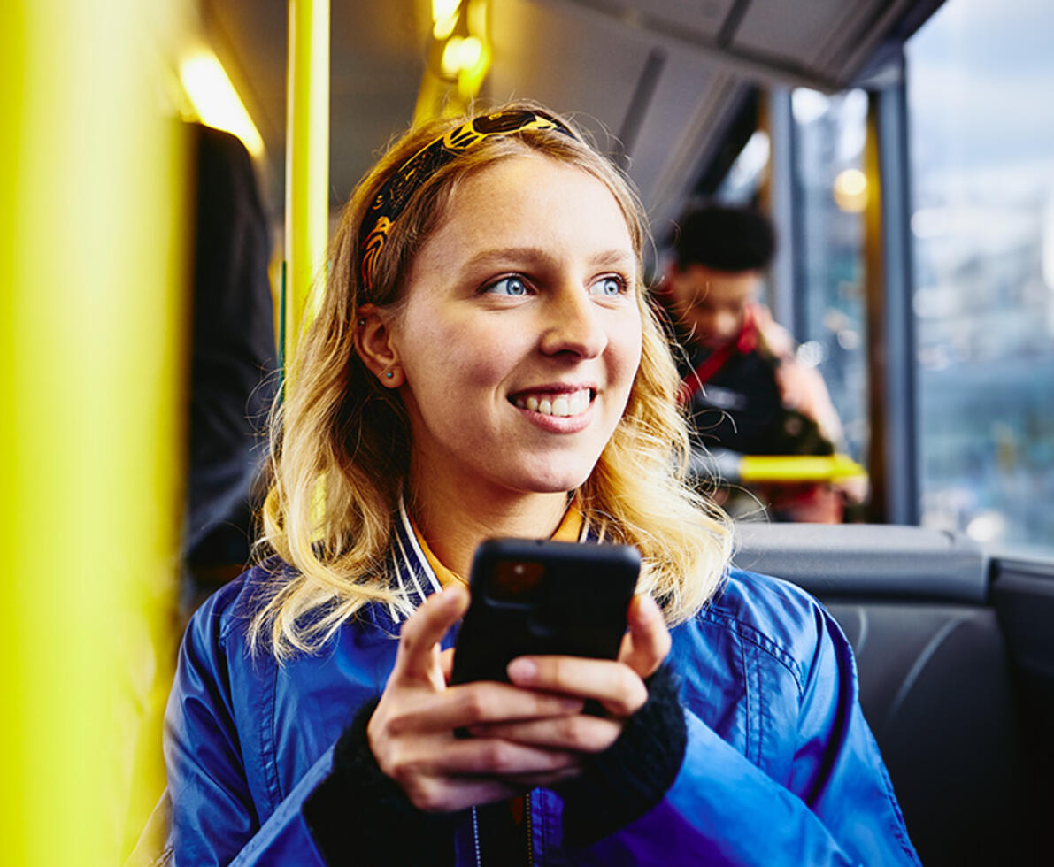 an image of a woman on a bus, smiling while looking out the window and holding her phone an image of a woman on a bus, smiling while looking out the window and holding her phone